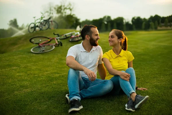 Unga vackra paret sitter på gräset i parken. — Stockfoto