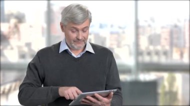 Olgun adam tipik haber dijital tablet üzerinde. PC tablet ofis pencere arka plan üzerinde kullanma dostu komuta sizde. Üst düzey kişiler ve modern teknoloji.