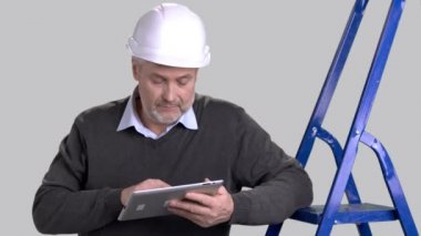 Beyaz Foreman'ı bilgisayar tablet kullanma. Olgun Oluşturucu'kask pc Tablet gri arka plan üzerinde çalışıyor. İnsanlar, inşaat, bakım.