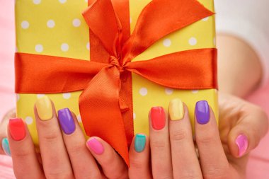 Parlak Hediyelik kutu kadın elinde. Kadın el hediye ile sarı kutu tutan çok renkli yaz çivi ile kapatın. Doğum günü hediye kutusu.