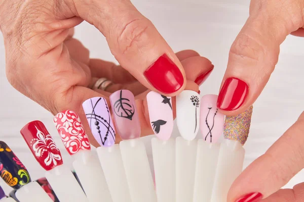 Manicured hands holding nail art samples.