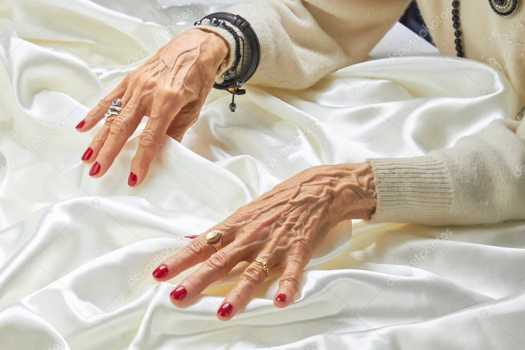 Hands with red nails on white silk.