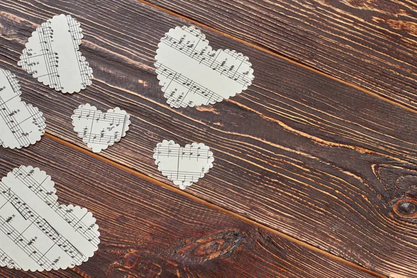Paper hearts with musical notes on wood.