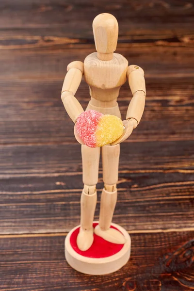 Wooden dummy holding heart-shaped candy.