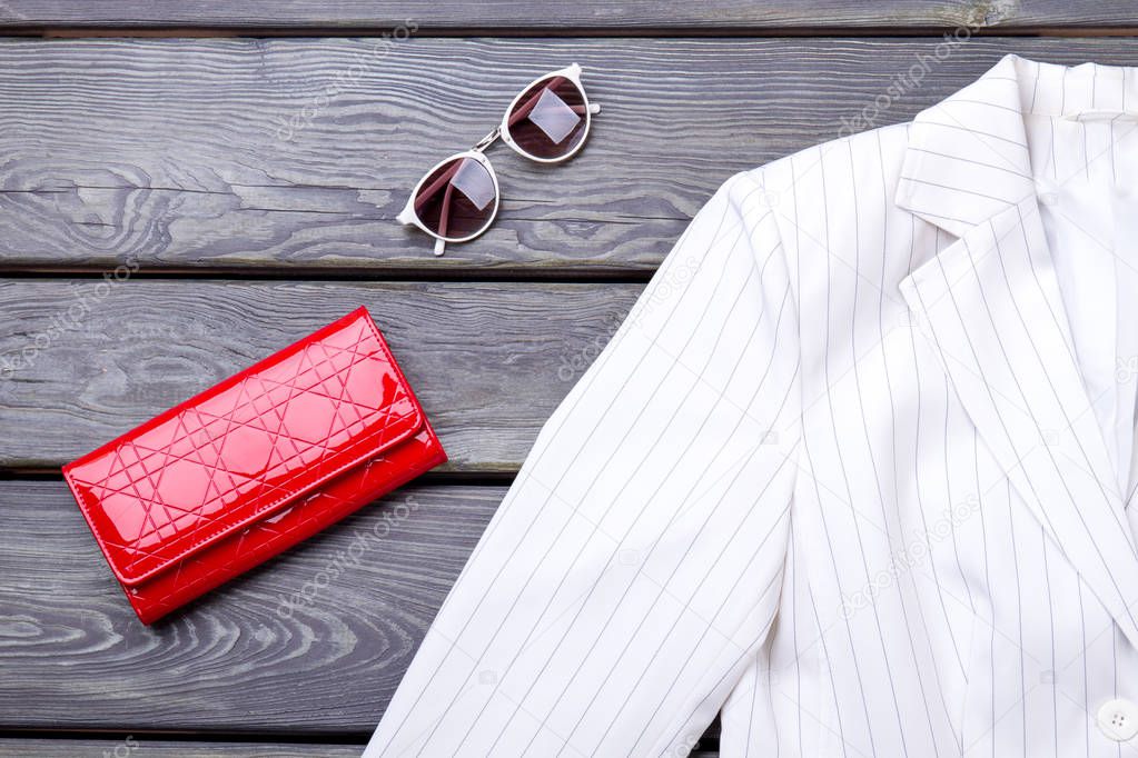 Close up white jacket, red wallet and sunglasses.