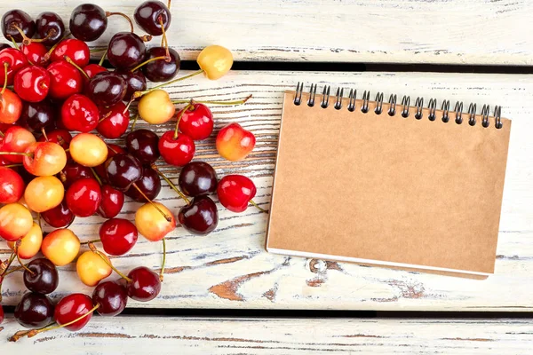 Cerezas surtidas y cuaderno de papel cerrado . — Foto de Stock