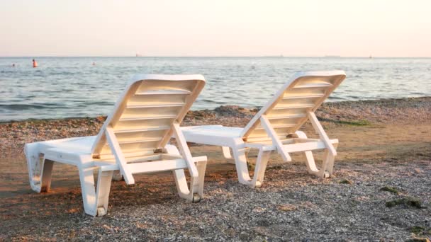 Two plastic chaise longues on seashore. — Stock Video