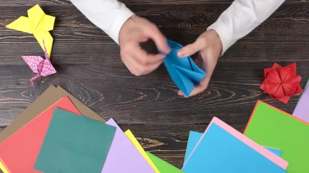 Manos masculinas creando origami con papel azul, vista superior . — Vídeo de stock