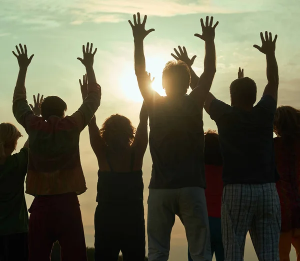 La gente se para contra un sol con las manos levantadas . — Foto de Stock