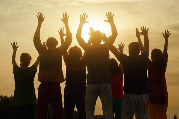 Happy family raised hands up on the sky at sunset.