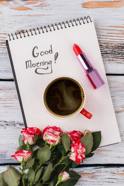 Good morning wish, coffee, flowers and lipstick. Top view, flat lay. White wood background.