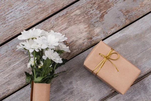 Ramo de flores de manzanilla y regalo envuelto en papel . — Foto de Stock