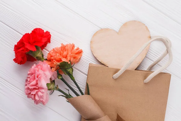 Rose flowers and shoppign bag. Wooden heart. White wood background.