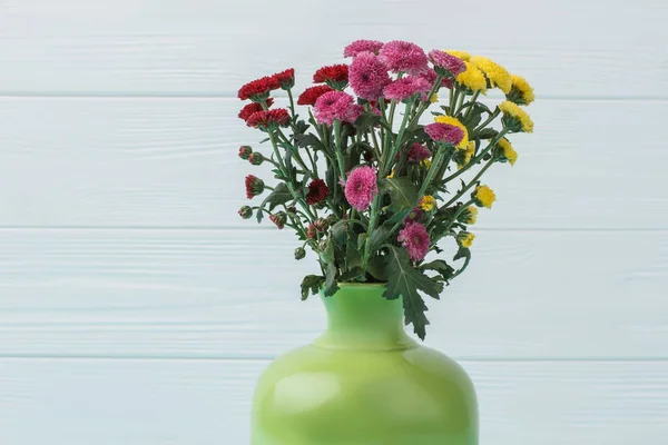 Multicolored chrysanthemum flowers in a green vase.