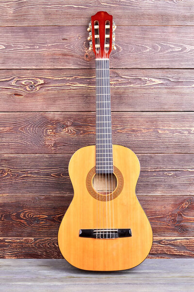 Acoustic guitar on wooden background. Yellow guitar on brown textured background. Classical stringed instrument.
