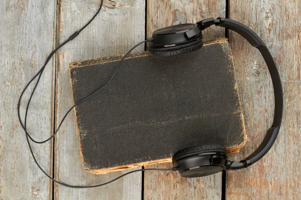 Sluchátka a kniha o dřevěné pozadí. — Stock fotografie