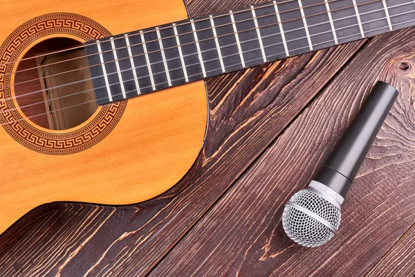 Acoustic guitar and microphone on wooden background.