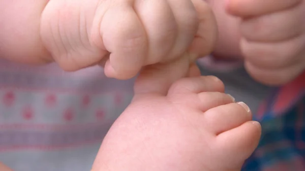 Baby hand grabbing feet close up.
