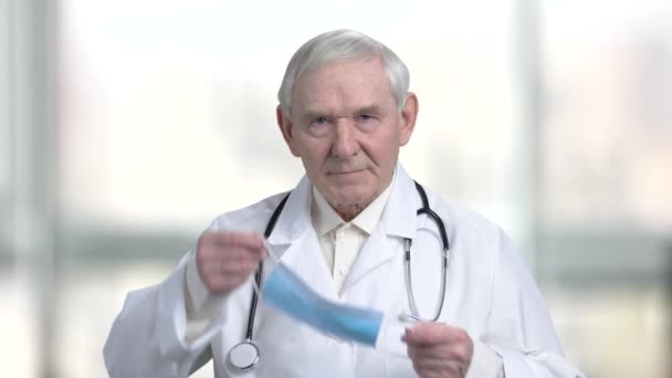 Viejo doctor poniéndose una máscara médica azul . — Vídeo de stock