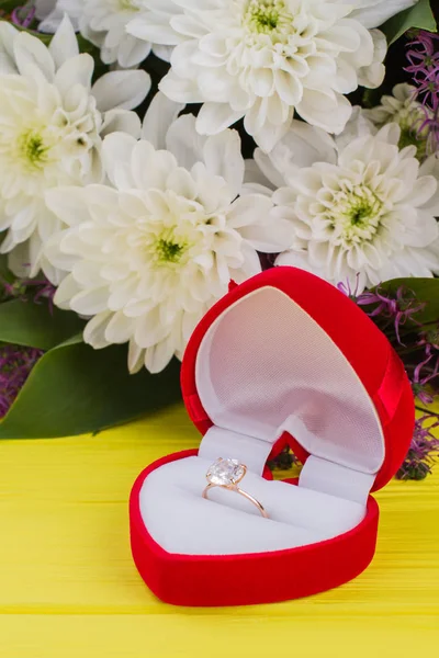 Engagement ring in red box and flowers.