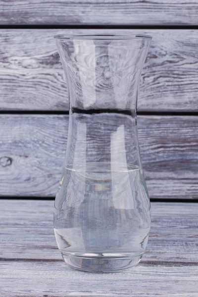 Clear glass vase with water on wooden background.