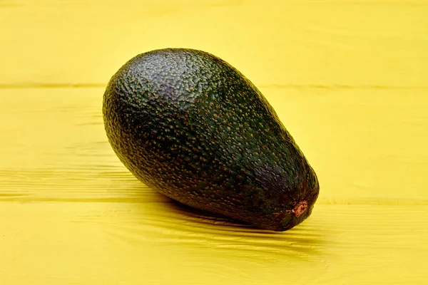 Aguacate entero sobre fondo amarillo de madera. — Foto de Stock