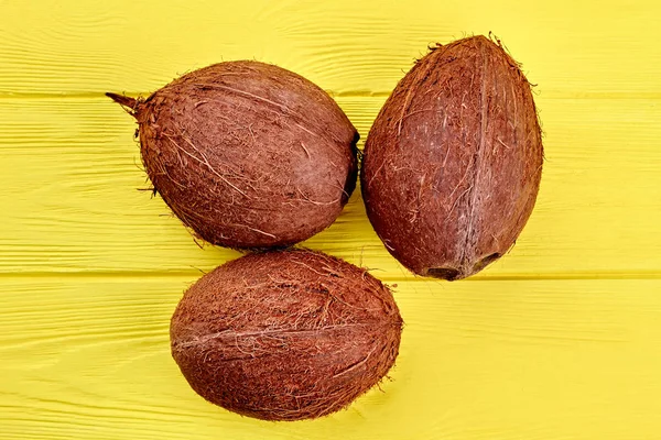 Drei ganze Kokosnüsse auf gelbem Holzgrund. — Stockfoto