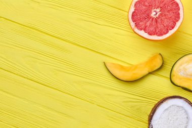 Tropikal meyve ve kopya alanı dilimlenmiş. Taze sulu greyfurt, mango ve Hindistan cevizi metin alanı olan sarı ahşap yüzeyde.