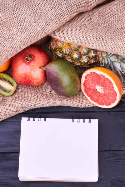 Exotic fruits and blank notepad, top view.