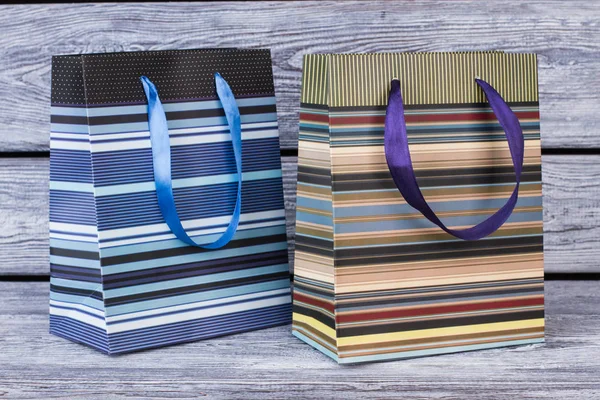Two striped shopping bags on wooden background.