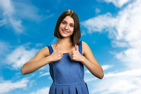 Attractive girl giving thumbs up on sky background. — Stock Photo, Image