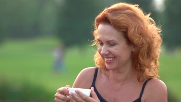 Счастливая улыбающаяся женщина пьет чай на открытом воздухе . — стоковое видео