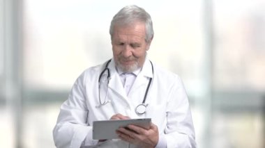 Pc tablet ile yaşlı doktor gülümseyerek. Neşeli beyaz doktor bilgisayar tablet bulanık arka plan kullanma.