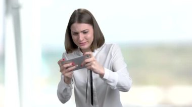 Genç komik kadın Smartphone oyun oynama. Neşeli kız beyaz bluz dokunmatik ekran telefonda online oyun oynarken arka plan bulanık.