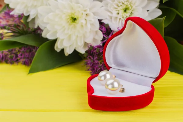 Heart-shaped box with earring and flowers.