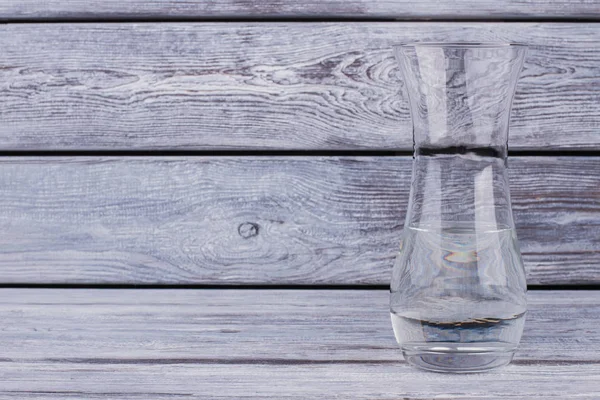 Glase vase with water on wooden background.