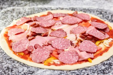 Pişmemiş pizza dilimlenmiş salam, jambon ve sosis ile.