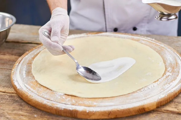 Chef mano spalmare salsa bianca su base di pizza con cucchiaio . — Foto Stock