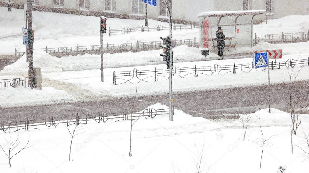 Woman is waiting for the bus during snow storm.