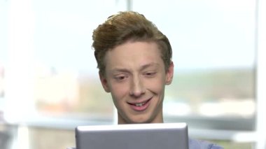 Beyaz genç çocuk tablet pc yolu ile konuşuyor. Dijital tablet kullanarak video konferans sahip yakışıklı ergen çocuk. Bulanık pencere arka plan.