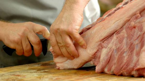 Primer plano de manos de carniceros cortando cerdo en carnicería . — Foto de Stock