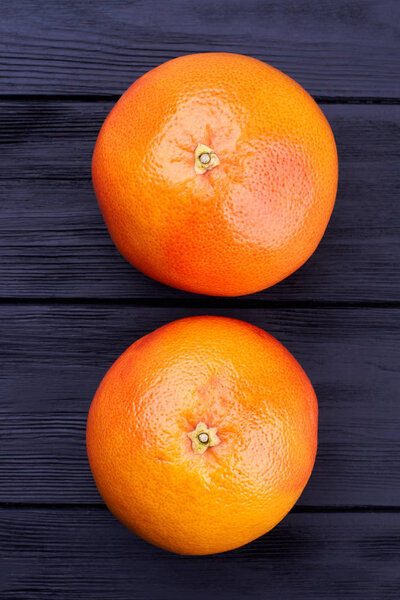Two whole grapefruits on dark background.