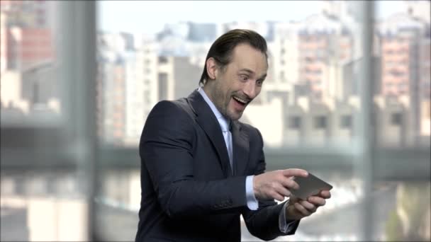 Cheerful businessman playing game on phone in office. — Stock Video