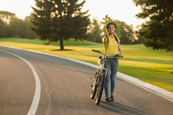 Happy girl with bicycle giving thumb up gesture.