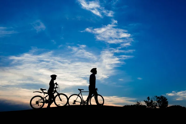 Silhouettes de jeune couple avec vélos au coucher du soleil . — Photo