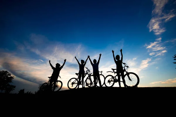 Quatre cyclistes avec les mains levées au coucher du soleil . — Photo