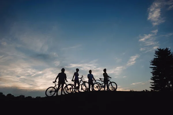 Cztery rowerzysta na wzgórzu na wieczornym niebie. — Zdjęcie stockowe