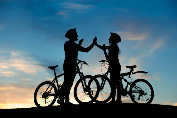 Весела пара велосипедистів плескає руками під час заходу сонця . — стокове фото