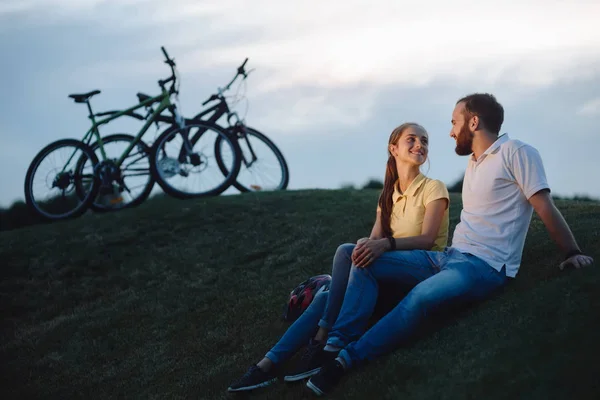 Pareja de ciclistas enamorados descansando en una colina verde . — Foto de Stock