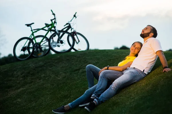 Romantyczna para siedzi na zielonej łące o zachodzie słońca. — Zdjęcie stockowe